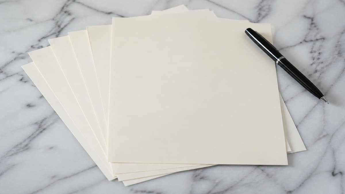 Printed resume drafts fanned on a white desk beside a laptop, highlighter, and a paper cup of coffee